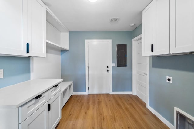 laundry area with electric dryer hookup, light hardwood / wood-style floors, electric panel, and cabinets