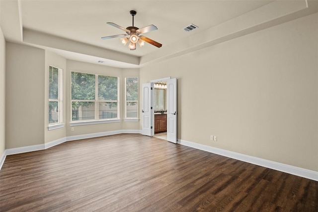 unfurnished room featuring a raised ceiling, dark wood-type flooring, and ceiling fan