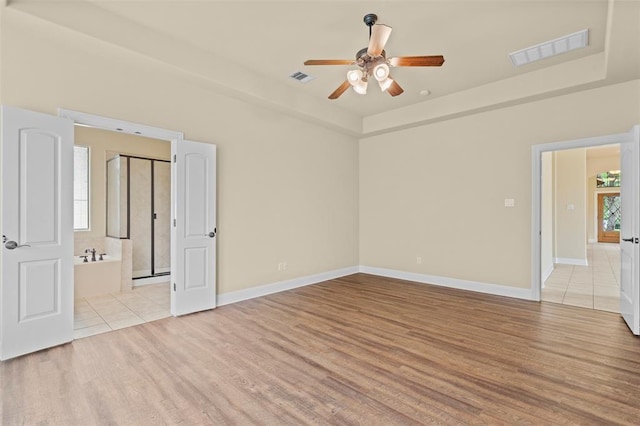 empty room with light hardwood / wood-style flooring, a raised ceiling, and ceiling fan