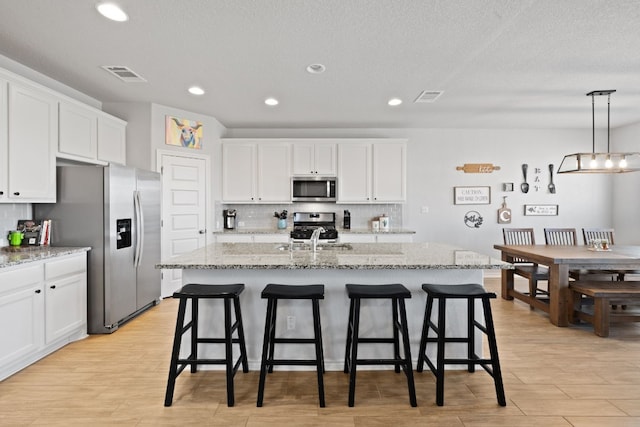 kitchen featuring white cabinetry, sink, hanging light fixtures, stainless steel appliances, and a center island with sink