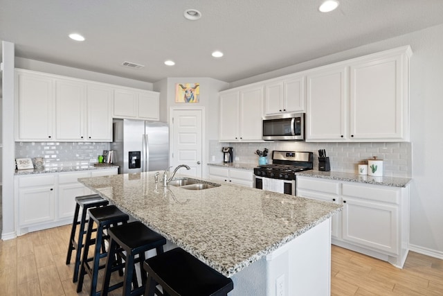 kitchen with stainless steel appliances, white cabinetry, sink, and a kitchen island with sink