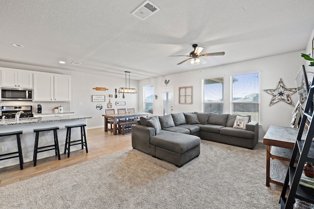 living room featuring sink, a textured ceiling, ceiling fan, and light hardwood / wood-style floors