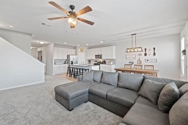 living room with ceiling fan, light colored carpet, and sink