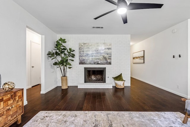 living room with dark wood-type flooring, ceiling fan, and a brick fireplace