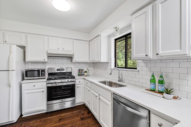 kitchen with appliances with stainless steel finishes, dark hardwood / wood-style floors, white cabinetry, sink, and decorative backsplash