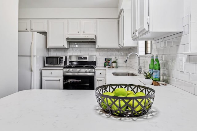 kitchen featuring sink, stainless steel appliances, tasteful backsplash, light stone countertops, and white cabinets