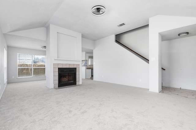 unfurnished living room featuring a tiled fireplace, vaulted ceiling, and light carpet