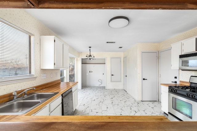 kitchen with appliances with stainless steel finishes, pendant lighting, white cabinetry, sink, and a chandelier