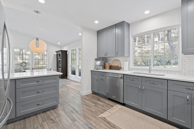 kitchen with sink, light wood-type flooring, appliances with stainless steel finishes, gray cabinets, and pendant lighting