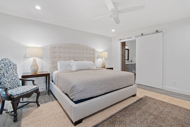 bedroom featuring ceiling fan, a barn door, connected bathroom, and light hardwood / wood-style floors