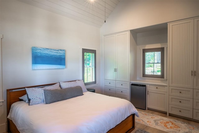 bedroom with lofted ceiling, light hardwood / wood-style floors, and stainless steel refrigerator