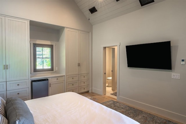 bedroom featuring ensuite bathroom, vaulted ceiling, stainless steel refrigerator, and light wood-type flooring