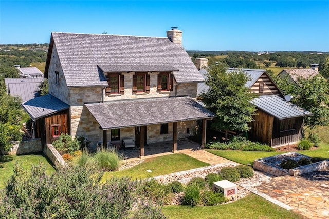 view of front of property featuring stone siding, metal roof, a chimney, and a standing seam roof