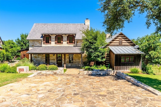 view of front of property with a standing seam roof, stone siding, a chimney, and metal roof