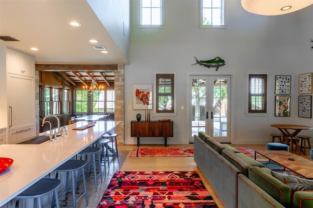 living room with french doors, a towering ceiling, light hardwood / wood-style floors, and sink