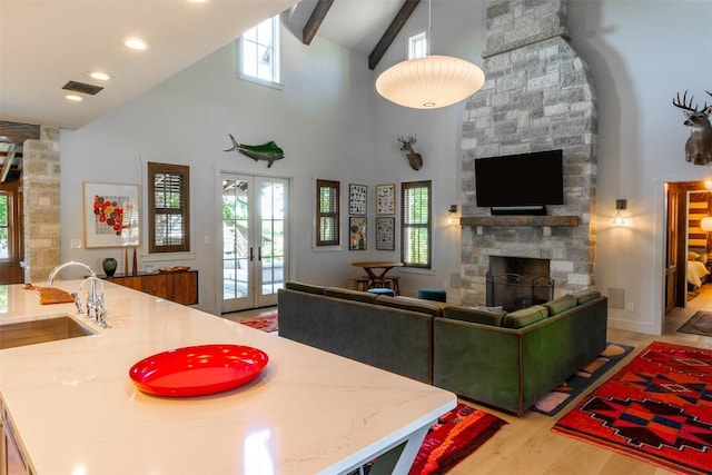 living room with french doors, sink, beam ceiling, light wood-type flooring, and a fireplace