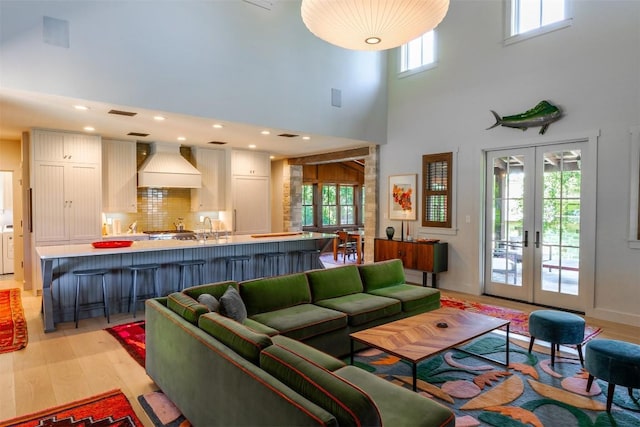 living room featuring sink, a towering ceiling, french doors, and light wood-type flooring