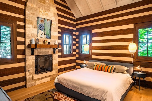 bedroom with wood-type flooring, a stone fireplace, lofted ceiling, and wooden walls