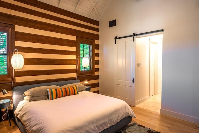 bedroom with multiple windows, wood-type flooring, a barn door, and vaulted ceiling