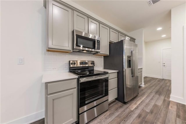 kitchen with tasteful backsplash, stainless steel appliances, gray cabinets, and hardwood / wood-style floors