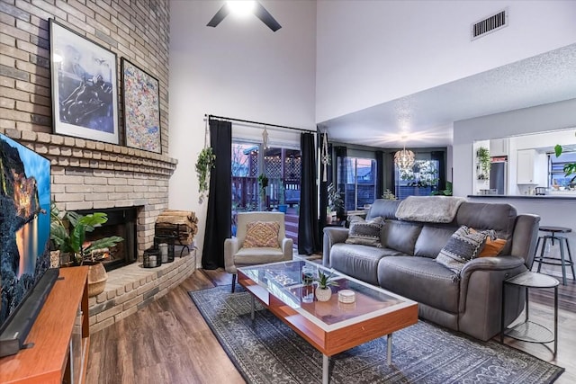 living room featuring ceiling fan, a fireplace, hardwood / wood-style floors, and a towering ceiling