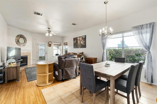 dining area with ceiling fan with notable chandelier, a tile fireplace, and light wood-type flooring