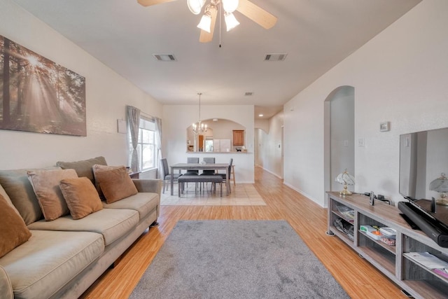 living room with visible vents, arched walkways, light wood-style floors, and ceiling fan with notable chandelier