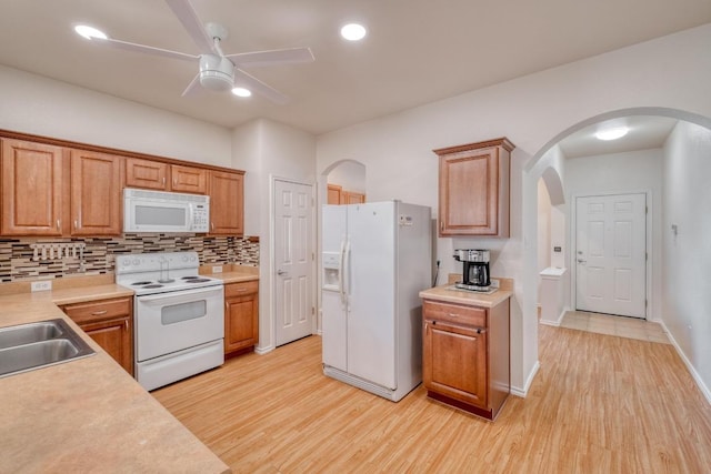 kitchen featuring white appliances, a ceiling fan, arched walkways, light wood-style floors, and backsplash