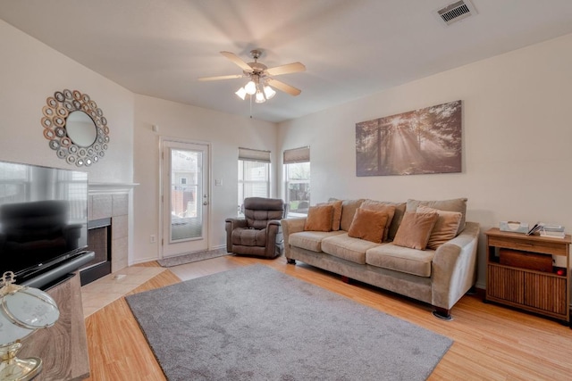 living area with a fireplace, light wood-style floors, visible vents, and ceiling fan