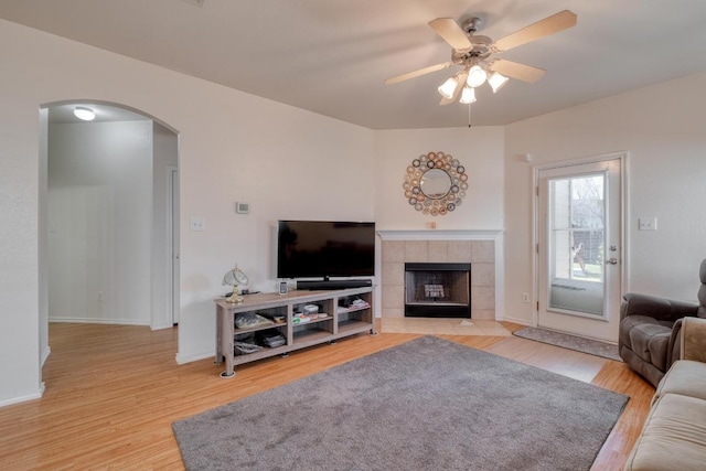 living area featuring light wood-style flooring, a ceiling fan, arched walkways, a fireplace, and baseboards