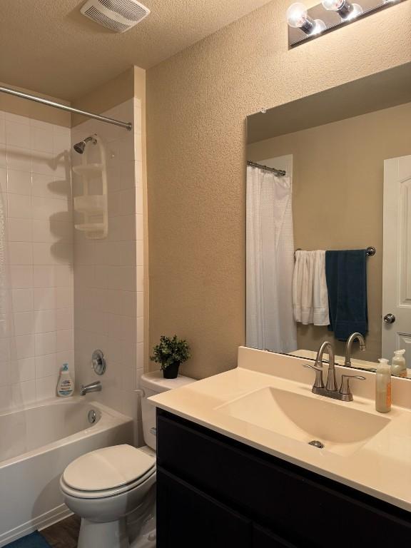 full bathroom featuring shower / bathtub combination with curtain, vanity, toilet, and a textured ceiling