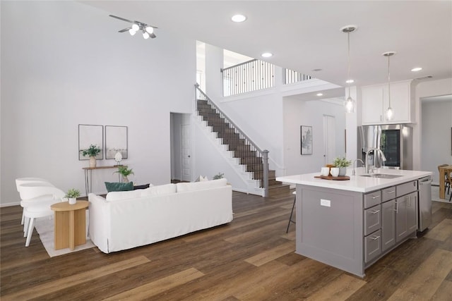 kitchen with dark hardwood / wood-style floors, stainless steel appliances, decorative light fixtures, and an island with sink