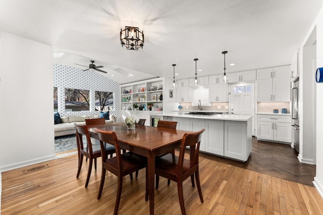 dining room featuring vaulted ceiling, sink, ceiling fan with notable chandelier, and a textured ceiling