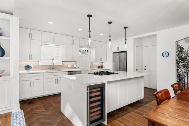 kitchen featuring sink, appliances with stainless steel finishes, a kitchen island, beverage cooler, and white cabinets