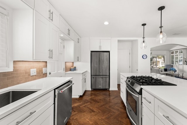 kitchen with pendant lighting, appliances with stainless steel finishes, white cabinetry, backsplash, and dark parquet flooring