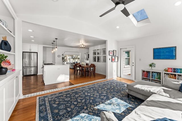 living room featuring vaulted ceiling with skylight, dark hardwood / wood-style flooring, and ceiling fan with notable chandelier