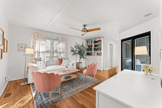 living room featuring hardwood / wood-style flooring, ceiling fan, and a textured ceiling