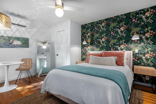 bedroom featuring ceiling fan, wood-type flooring, and an AC wall unit