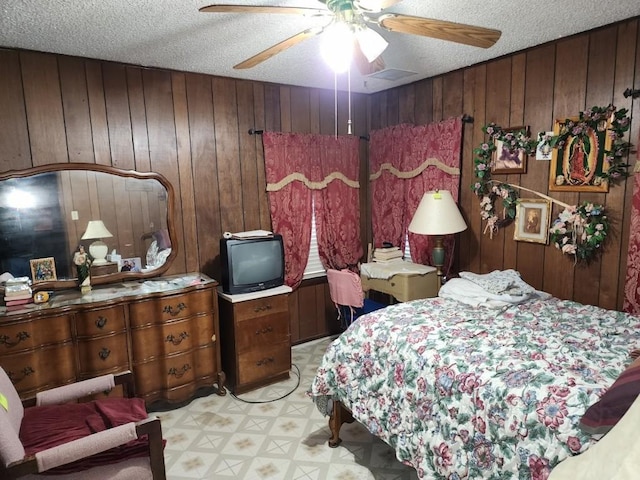 bedroom featuring ceiling fan, wooden walls, and a textured ceiling