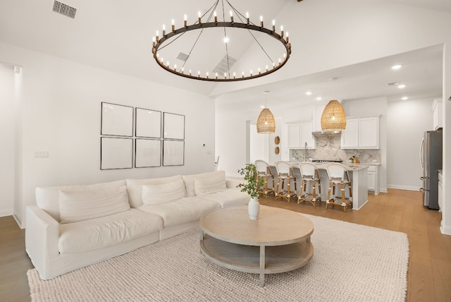 living room featuring a notable chandelier, high vaulted ceiling, sink, and light wood-type flooring