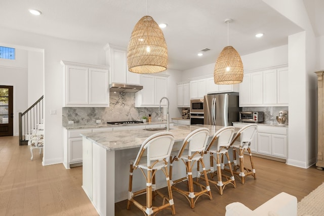 kitchen featuring stainless steel appliances, white cabinets, and a center island with sink