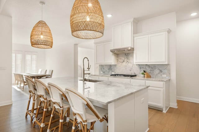 kitchen with sink, stainless steel gas cooktop, an island with sink, pendant lighting, and white cabinets