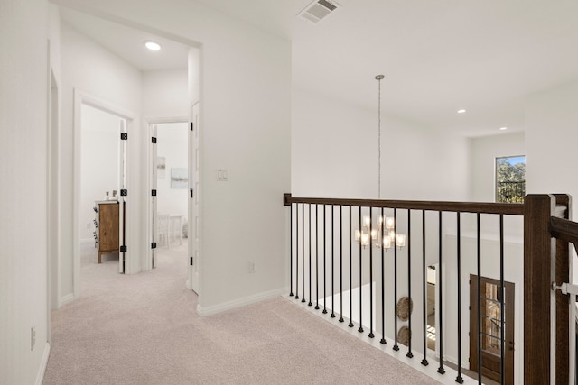 hallway with light carpet and a chandelier