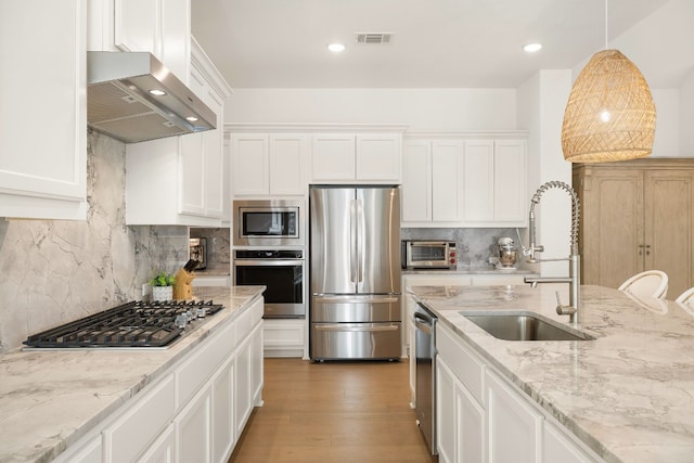 kitchen featuring white cabinetry, stainless steel appliances, range hood, and sink