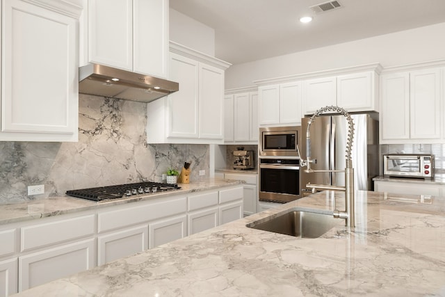 kitchen featuring backsplash, stainless steel appliances, light stone countertops, and white cabinets