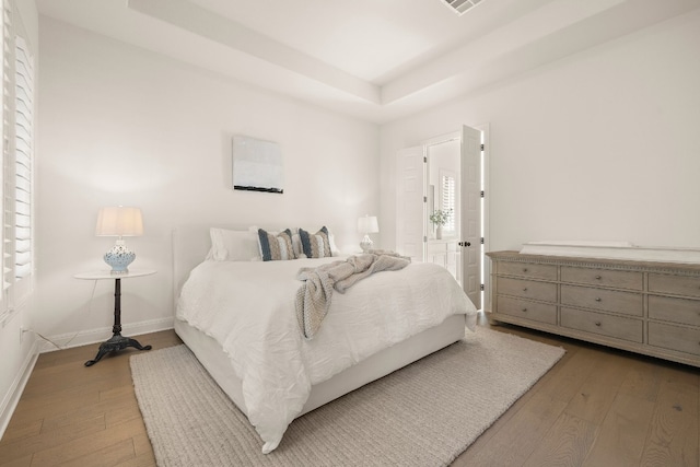 bedroom with a raised ceiling and light wood-type flooring