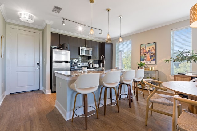 kitchen with crown molding, appliances with stainless steel finishes, dark brown cabinetry, wood-type flooring, and a kitchen bar