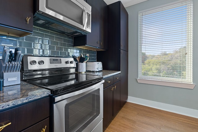 kitchen featuring dark brown cabinets, light wood-type flooring, dark stone countertops, appliances with stainless steel finishes, and decorative backsplash