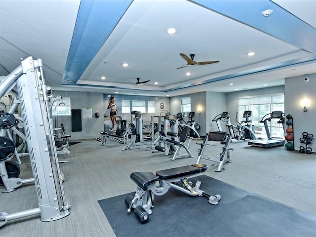 workout area with ceiling fan and a tray ceiling