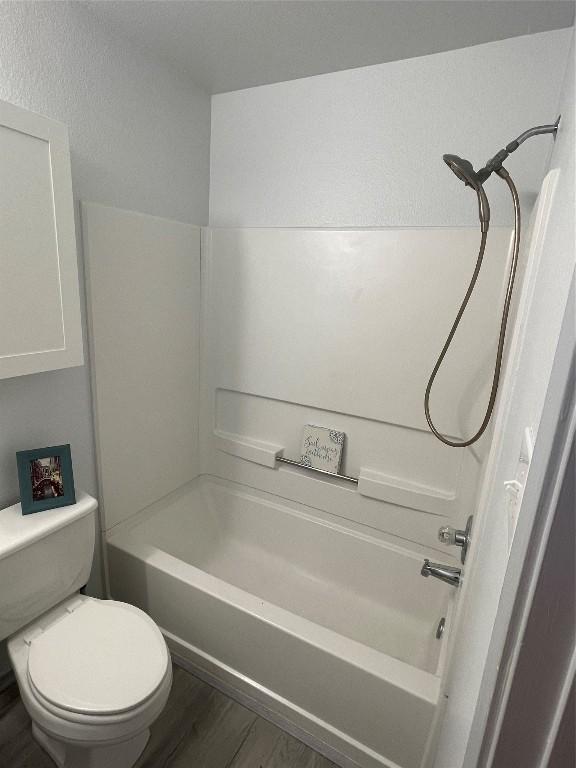 bathroom featuring shower / washtub combination, hardwood / wood-style floors, and toilet